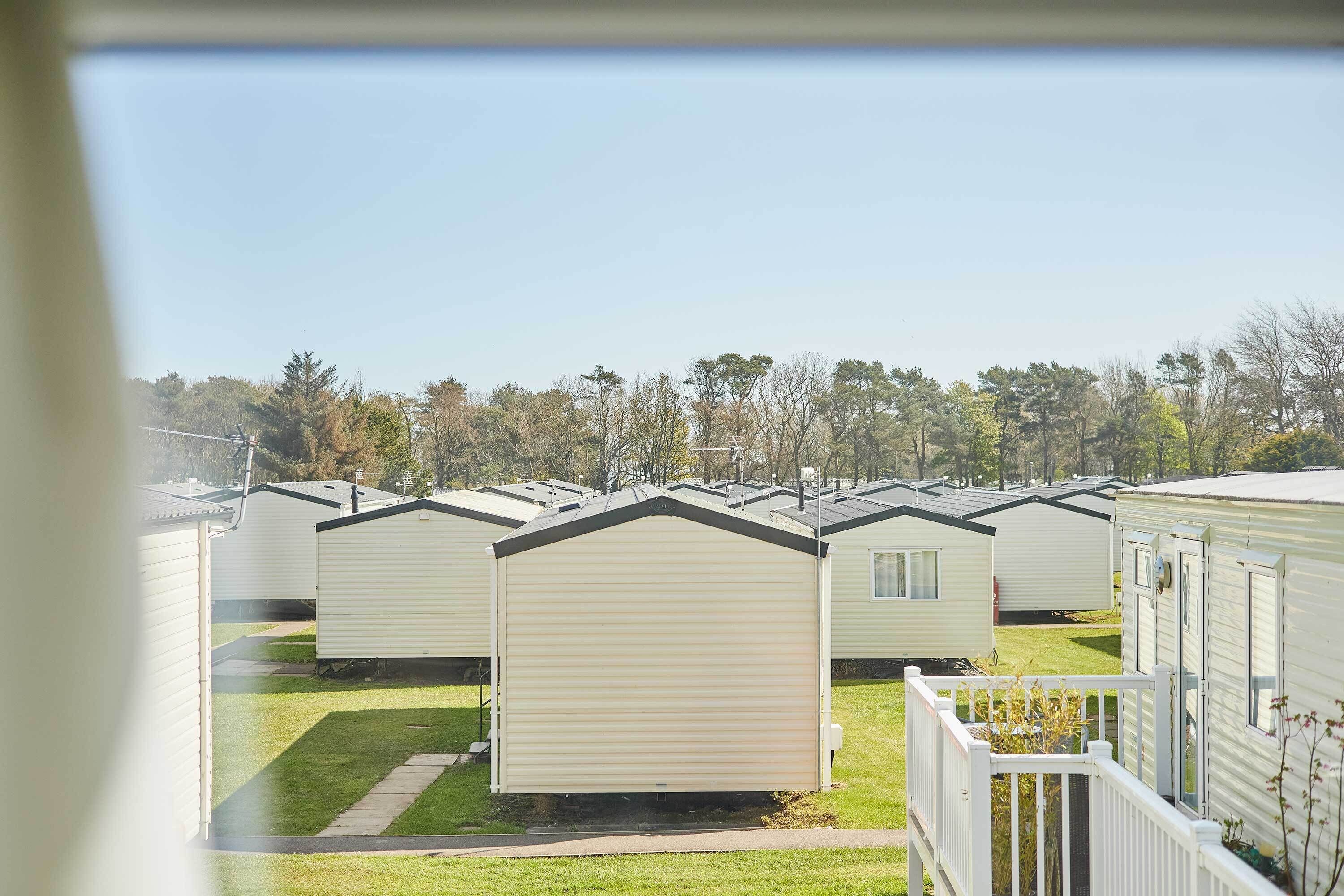 A row of mobile homes with a grassy yard and trees in the background.