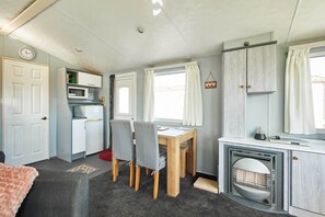 A compact kitchen with a microwave, a dining table with chairs, a small cabinet, and a fireplace.