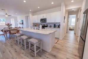 Una cocina moderna con armarios blancos, una isla de mármol y un comedor con sillas de madera y un jarrón de flores.