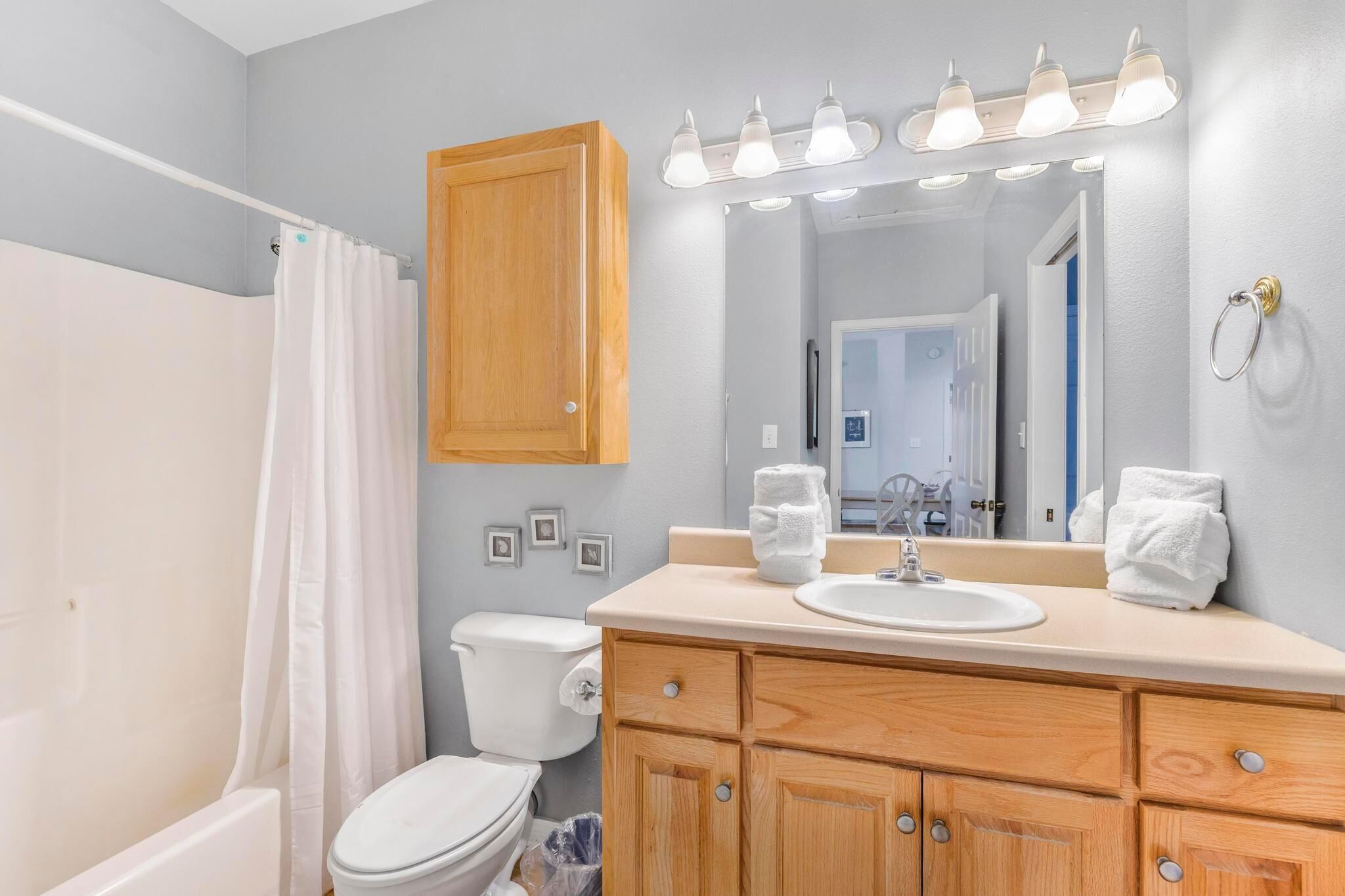A bathroom with a shower, toilet, vanity with a sink, mirror, and light fixture.