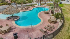 A swimming pool with a curved edge, surrounded by lounge chairs and tables, and a thatched umbrella. - The Rookery 3602 (Gulf Shores)
