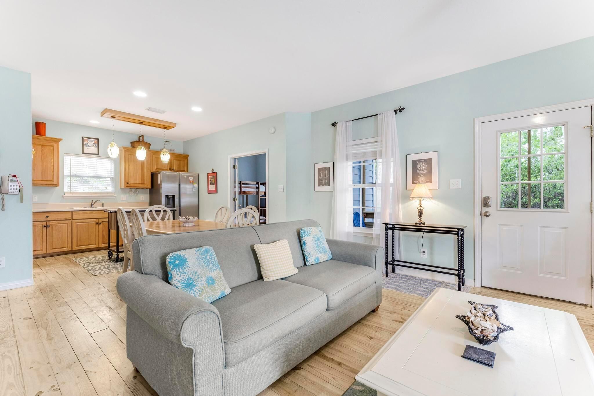 A living room with a grey sofa, wooden cabinets, a dining table, and a kitchen in the background.