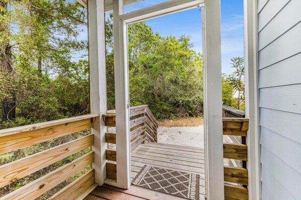 A wooden deck leading to a beach with a view of dense greenery.
