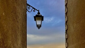 Un patio empedrado con un muro de ladrillo, un farol metálico y vistas a colinas ondulantes bajo un cielo despejado.