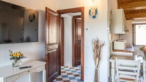 Un pasillo con piso a cuadros, una puerta de madera, un reloj de pared y una zona de cocina con armarios y un tostador.