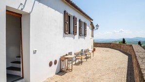 Un edificio blanco con un balcón, contraventanas de madera y vistas al campo.