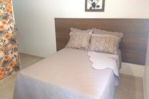 A bed with a wooden headboard, a floral curtain, and a framed picture on the wall. - Pousada Casa Guacuri (Itupeva)