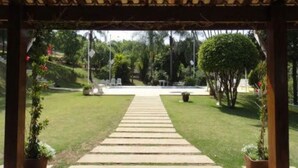 A covered walkway leading to a pool area with a view of a well-maintained lawn and trees. - Pousada Casa Guacuri (Itupeva)