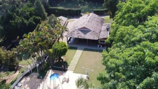 A house with a sloped roof, surrounded by lush greenery and a swimming pool. - Pousada Casa Guacuri (Itupeva)