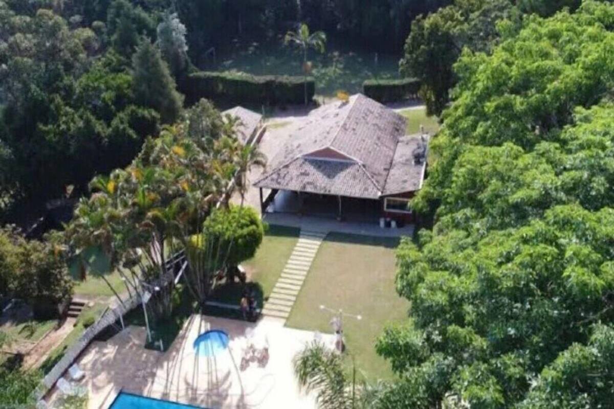 A house with a sloped roof, surrounded by lush greenery and a swimming pool.