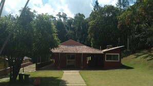 A red building with a tiled roof, surrounded by trees and a grassy area. - Pousada Casa Guacuri (Itupeva)