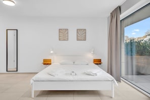 Ein modernes Hotelzimmer mit einem großen Bett, zwei Wandleuchten, einem großen Fenster mit Vorhängen und Blick ins Freie.