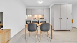 A modern kitchen with white cabinets, a dining table with four chairs, and a white wardrobe. - Neudorf Studio Near Kirchberg and Airport (Luxembourg)