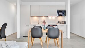 A modern kitchen with white cabinets, a microwave, and a dining area with a table and chairs. - Neudorf Studio Near Kirchberg and Airport (Luxembourg)