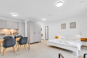 Moderni hotellihuone, jossa on sänky, yöpöytä ja näkymä keittiötilaan.