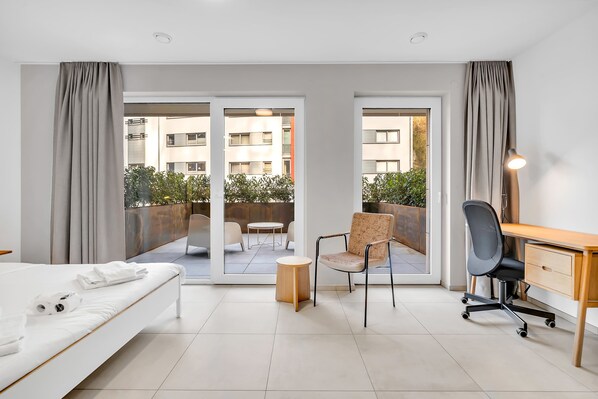 Ein Hotelzimmer mit Bett, Schreibtisch, Stuhl, kleinem Tisch und Blick auf den Balkon.