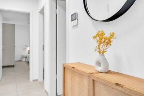 A hallway with a wooden console table, a vase with yellow flowers, a black-framed mirror, and a small device on the wall. - 2BR 2Bath Near Kirchberg and Airport (Luxembourg)