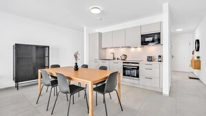 A modern kitchen with white cabinets, a wooden dining table, and black chairs. - Modern Studio in Neudorf Near Kirchberg (Luxembourg)