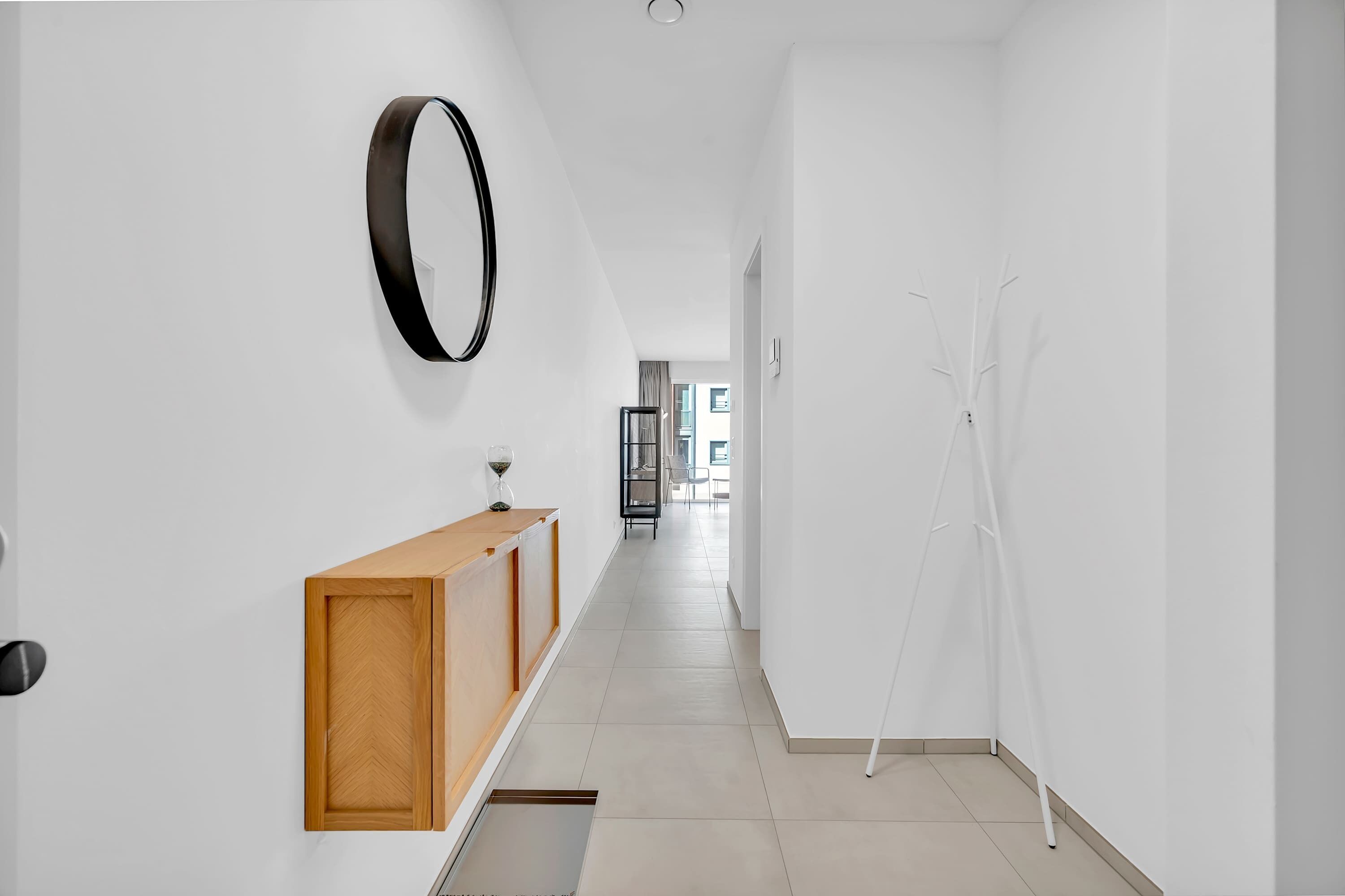 A hallway with a wooden cabinet, a wall-mounted mirror, and a white abstract sculpture.