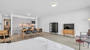 A modern hotel room with a bed, a desk, a dining area, a TV, and a wardrobe. - Modern Studio in Neudorf Near Kirchberg (Luxembourg)