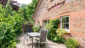 Ein Backsteinhaus mit einer Terrasse, ausgestattet mit einem Tisch und Stühlen, umgeben von viel Grün.