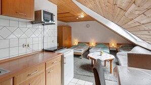 Ein kompakter Raum mit Küchenzeile, zwei Betten, einem kleinen Tisch und einer Decke mit Holzbalken.