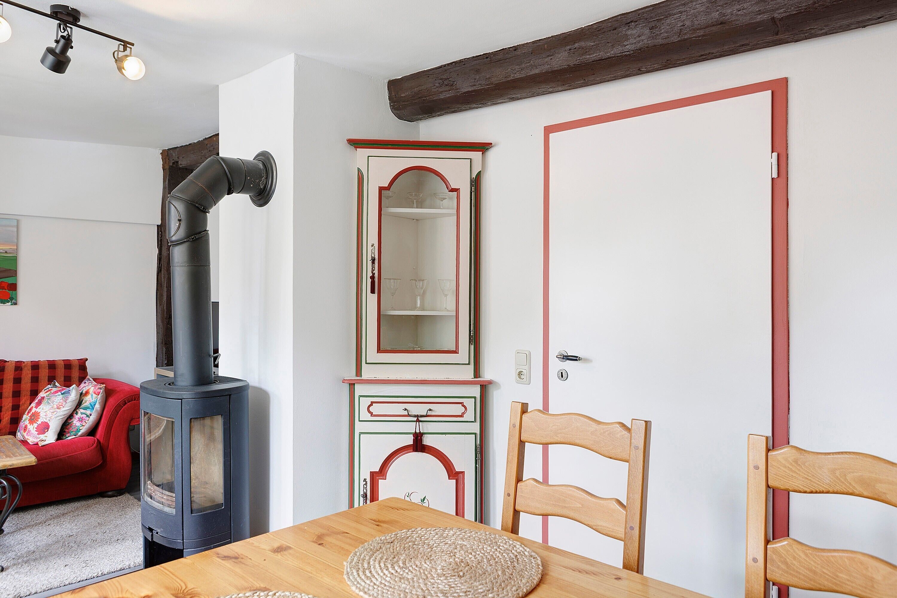 A cozy room with a wood-burning stove, a red sofa, a wooden dining table, and a mirror with a decorative frame.