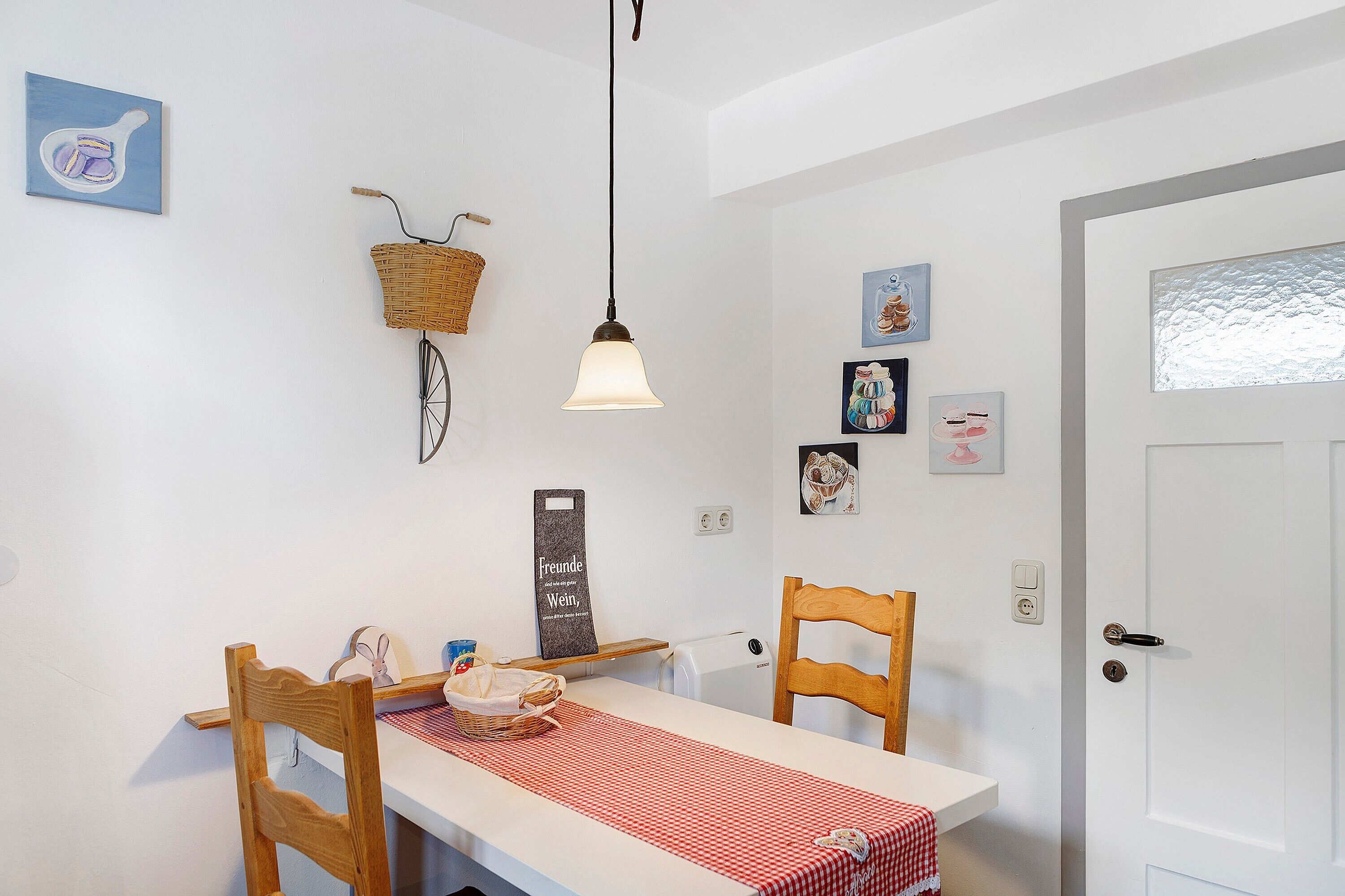 A dining area with a table, chairs, a hanging light, and wall decorations.