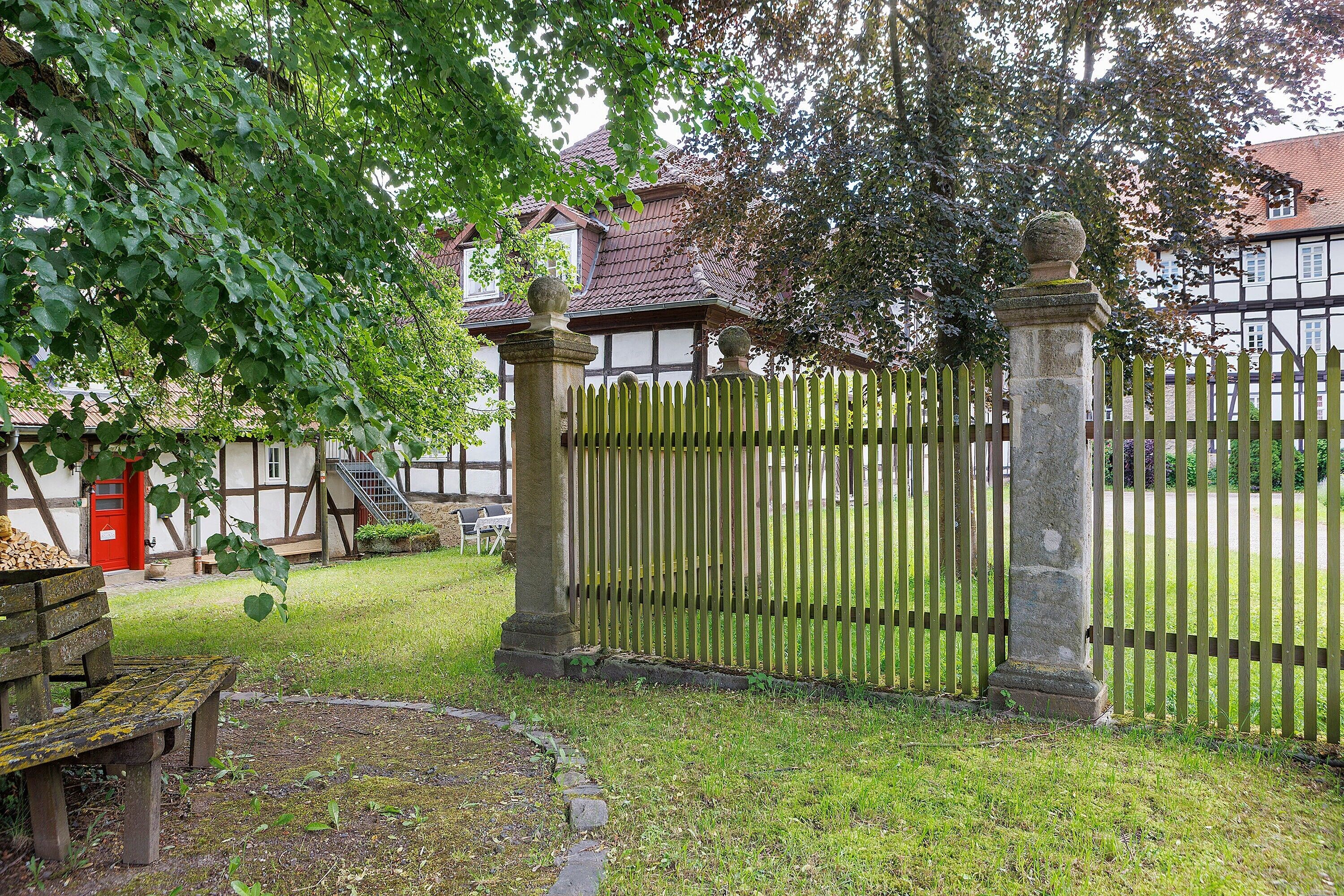 Ein traditionelles Gebäude mit Holzzaun, einer Bank und einer roter Tür.