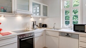 Una cocina moderna con armarios blancos, horno empotrado, lavavajillas, cafetera y microondas.
