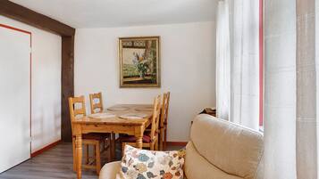 Een eetgedeelte met een houten tafel en stoelen, een schilderij aan de muur en een bank met een bloemenkussen.
