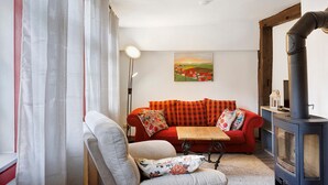 Una sala de estar acogedora con un sofá rojo, un sillón gris, una mesa de madera y un estufa de leña negra.