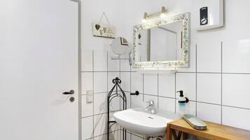 Un baño con lavamanos blanco, un espejo con marco floral, una pequeña estantería y un perchero para toallas.
