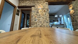A dining area with a wooden table, stone walls, and a kitchen in the background.