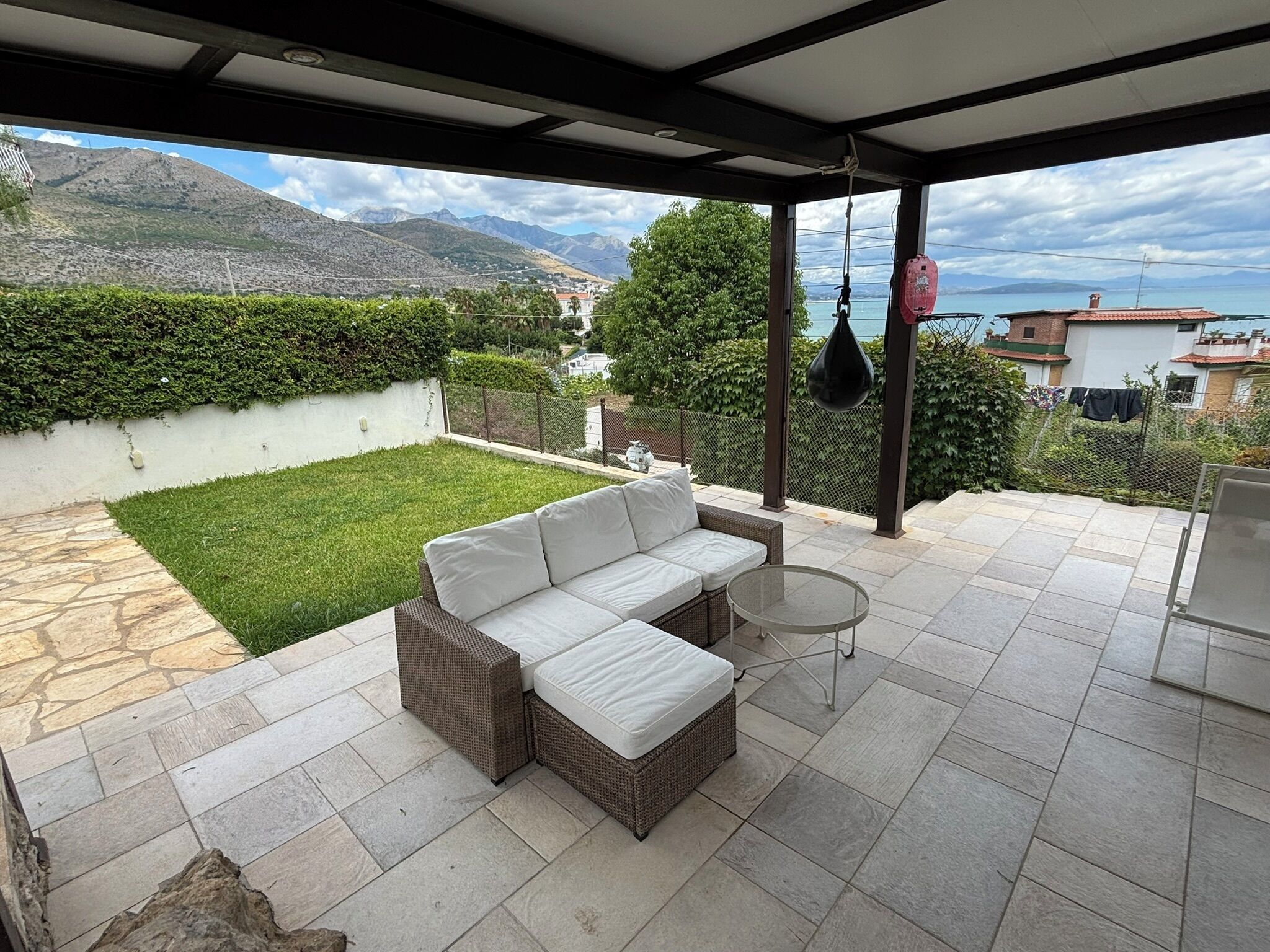 A covered outdoor patio with a white sofa, a small round table, and a hanging chair.