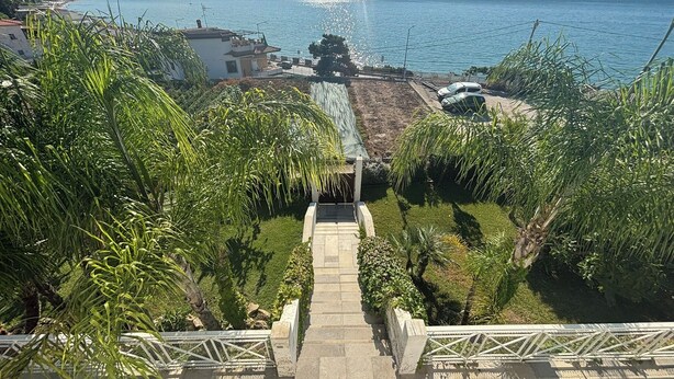 A coastal view with a staircase leading to a building, surrounded by greenery and a clear sky.