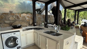 A kitchen with a built-in washing machine, a sink, and a stone wall backdrop.
