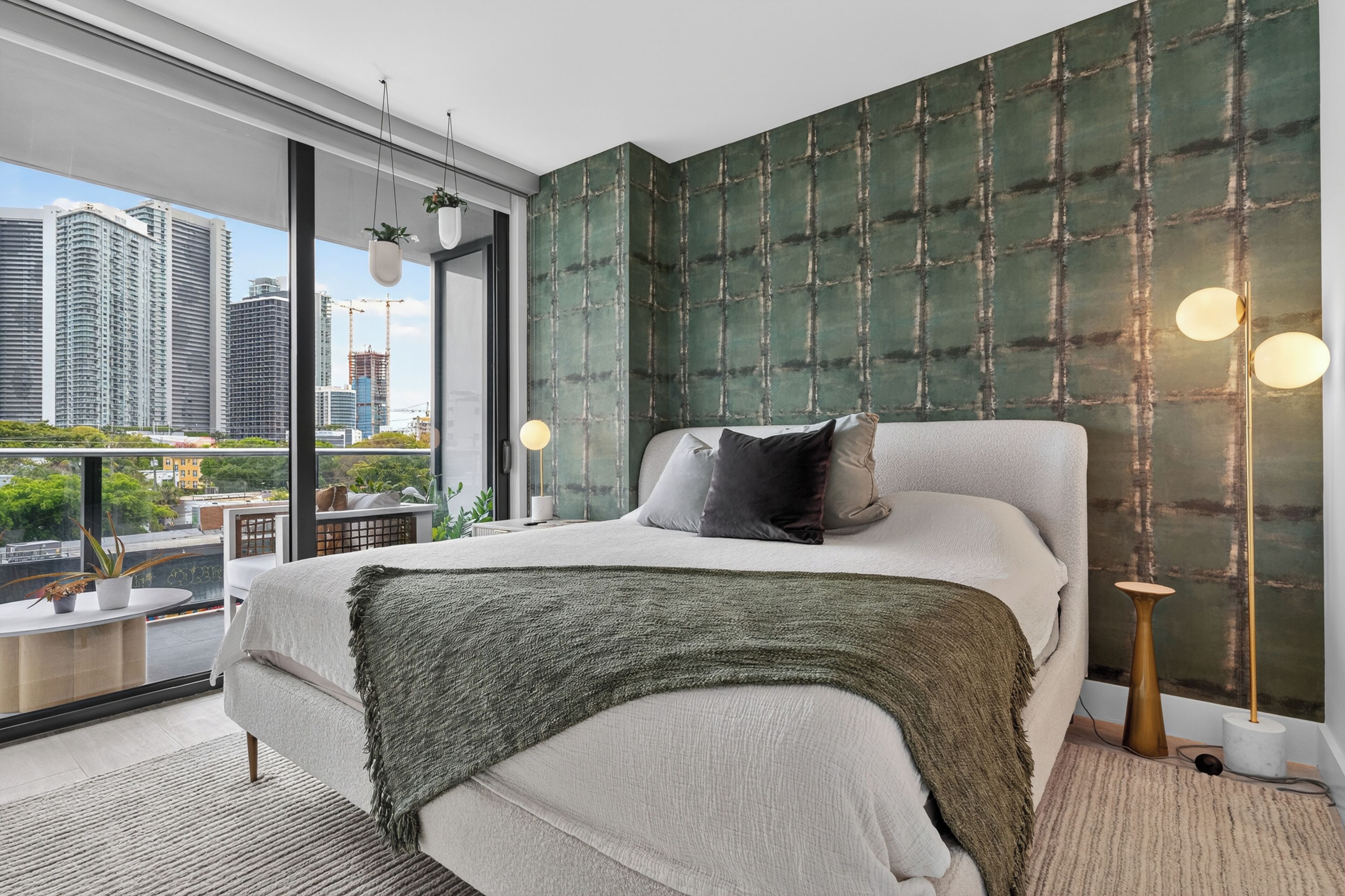Camera da letto moderna con un letto grande, vista sulla città e una parete verde con texture.