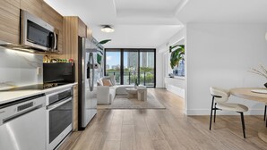 A modern kitchen with built-in appliances, a dining area with a round table and chairs, and a large window with a city view. - NEW! Luxury 1 BR Hyde Midtown Walk to Design District and Walk Evreywhere. (Miami)