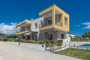 Un edificio residencial de dos pisos con balcones, una piscina y cielo despejado.