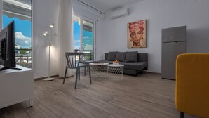 Ein modernes Wohnzimmer mit einer Couch, einem Esstisch mit Stühlen, einem Fernseher und einem Kühlschrank.