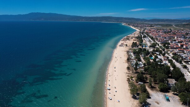 Ein Luftbild einer Küstenstadt mit Strand, klarem blauen Meer und Wohnhäusern.