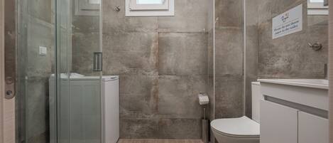 Un baño con cabina de ducha de vidrio, inodoro y lavamanos.