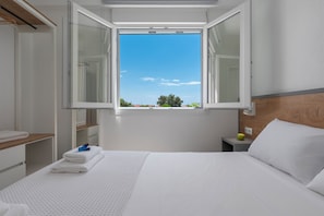 A hotel room with a bed, a nightstand, a window with an open view, and a wooden headboard. - SLV Danai 7 Apartments (Pangaio)