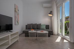 A modern living room with a flat-screen TV, a sofa, two round tables with geometric designs, and a large window with a view of greenery. - SLV Danai 7 Apartments (Pangaio)