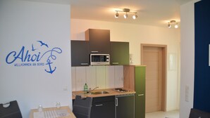 Een compact keukenblok met een magnetron, spoelbak en een kleine eethoek met een tafel en stoelen.