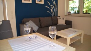 Een woonkamer met een bank, twee wijnglazen op een tafel en twee ingelijste foto's aan de muur.