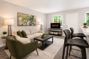 Un salon avec un canapé, des fauteuils, une table basse, un téléviseur et un tableau accroché au mur.