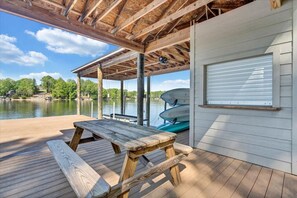 A wooden deck with a picnic table, a covered area, and boats docked by a lake.