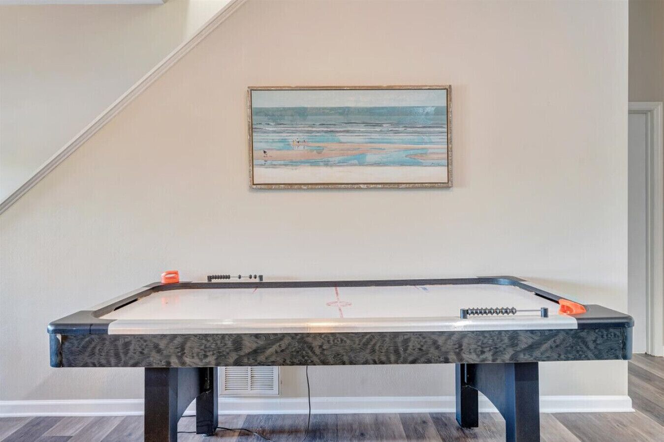 A pool table in a room with a staircase and a painting on the wall.